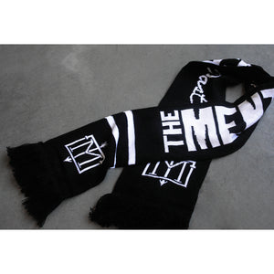 folded black and white scarf on a concrete floor. Menzingers T M emblem on the end next to the fringe