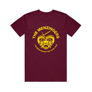 image of a maroon tee shirt on a white background. the tee shirt has a full center chest print in yellow of a heart with a sad face and tears and a mining pick in the top. arhced around the heart says the menzingers. arhced around at the bottom of the heart says i've been mining for your love
